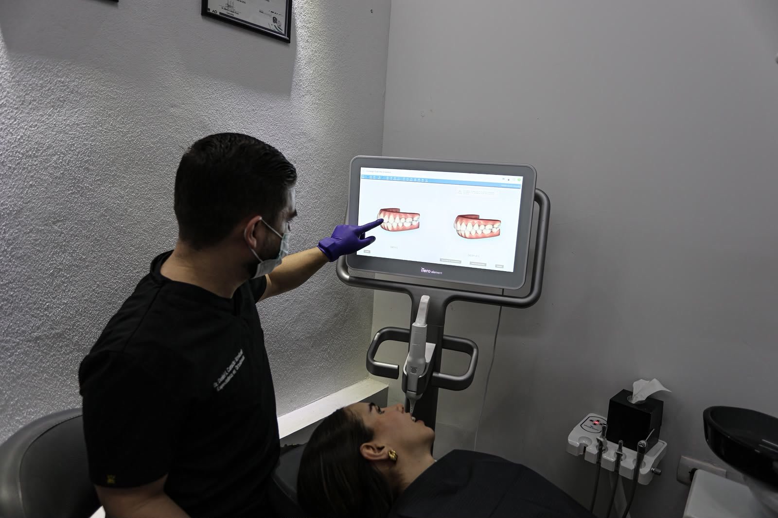 El doctor le muestra a una paciente su simulación de antes y después en la pantalla del escáner iTero